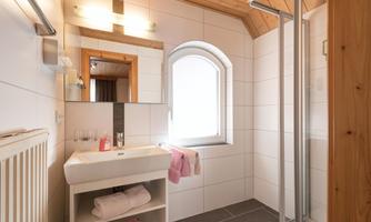 A modern bathroom with a shower and a sink. The walls are tiled in light colors, and the lighting creates a pleasant atmosphere.