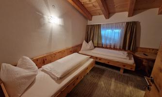 A cozy room with wooden decor and two single beds. The window is covered with a light curtain and there is soft light on the wall.
