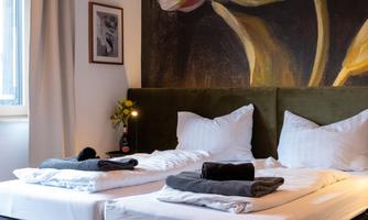 A modern bedroom with two beds and fresh towels. In the background, a large piece of art featuring a flower hangs.