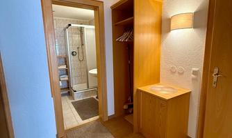 A bright hallway with a wooden wardrobe and a small table. In the background, a bathroom is visible.
