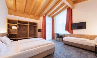 A modern room with a wooden ceiling and two beds. Large windows provide plenty of daylight.