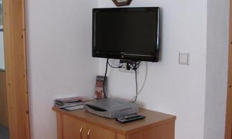A modern television on a wall. Below it, a wooden cabinet with numerous magazines.