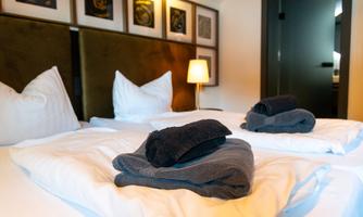 A cozy bedroom with two beds and decorative cushions. Fresh towels are placed on the blanket.