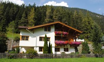 A beautiful house in the mountains with a blooming balcony.  
Surrounded by green forests and a clear blue sky.