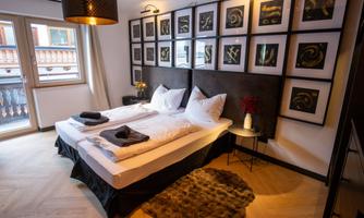 A modern bedroom with two beds and stylish wall art. Large windows provide daylight and a view outside.