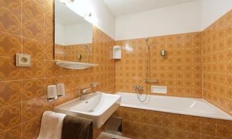 A bathroom with orange tiles and a bathtub. There is a sink, a mirror, and towels in neutral colors.