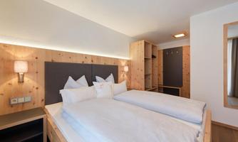 A modern bedroom with wooden paneling and a large double bed. The soft lighting creates a relaxed atmosphere.