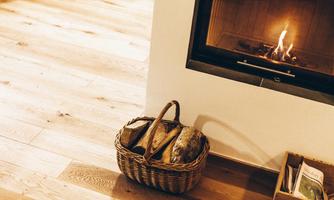 A basket made of wood stands next to a modern fireplace. The fireplace creates a cozy atmosphere with a gentle fire.
