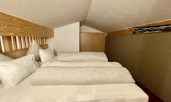 A cozy bedroom with two beds and bright pillows. The walls are painted in neutral colors and the ceiling is slanted.