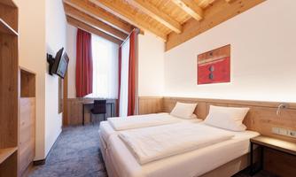 A modern hotel room with wooden ceilings and two separate beds. The room is friendly and bright, with a desk and a television.