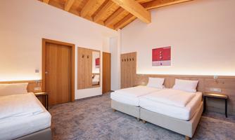 A modern hotel room with a wooden ceiling and two single beds. The room is bright and cheerfully designed, with a large mirror and a cozy atmosphere.