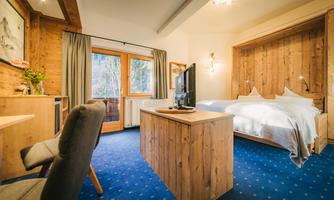 A cozy hotel room with wood paneling and two single beds. There are curtains at the window and a desk with a chair.