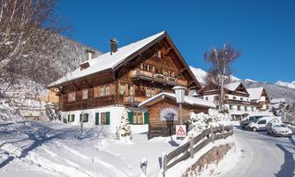 A traditional wooden house in the snow with a clear blue sky. The surroundings are wintry and picturesque.