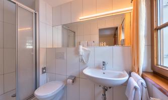 A modern bathroom with a shower, a sink, and a large mirror area. The walls are brightly tiled, and there are fresh towels.