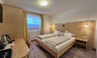 A modern hotel room with two beds and wooden interior. Large windows let in plenty of daylight.