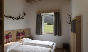 A cozy bedroom with two single beds and wooden details. The window offers a view of the green landscape outside.