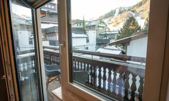 A cozy balcony overlooking snow-covered mountains and surrounding chalets. The windows are open, allowing fresh air to flow in.