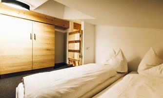 A cozy bedroom with two single beds and a wooden wardrobe. The walls are light, and the room feels inviting and warm.