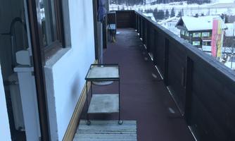 A balcony with a view of snow-capped mountains. On the right, there is a table with a tablecloth and a rug on the floor.