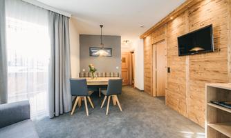 A modern living room with wooden walls and a cozy dining table. Large windows provide plenty of natural light.