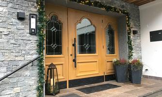 An inviting entrance with two large, decorative wooden doors and a stone wall. Green plants and a lantern give the space a cozy atmosphere.