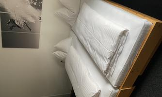A furnished bedroom with two single beds. The bed linen is white and fresh, and there is a picture of a skier hanging on the wall.