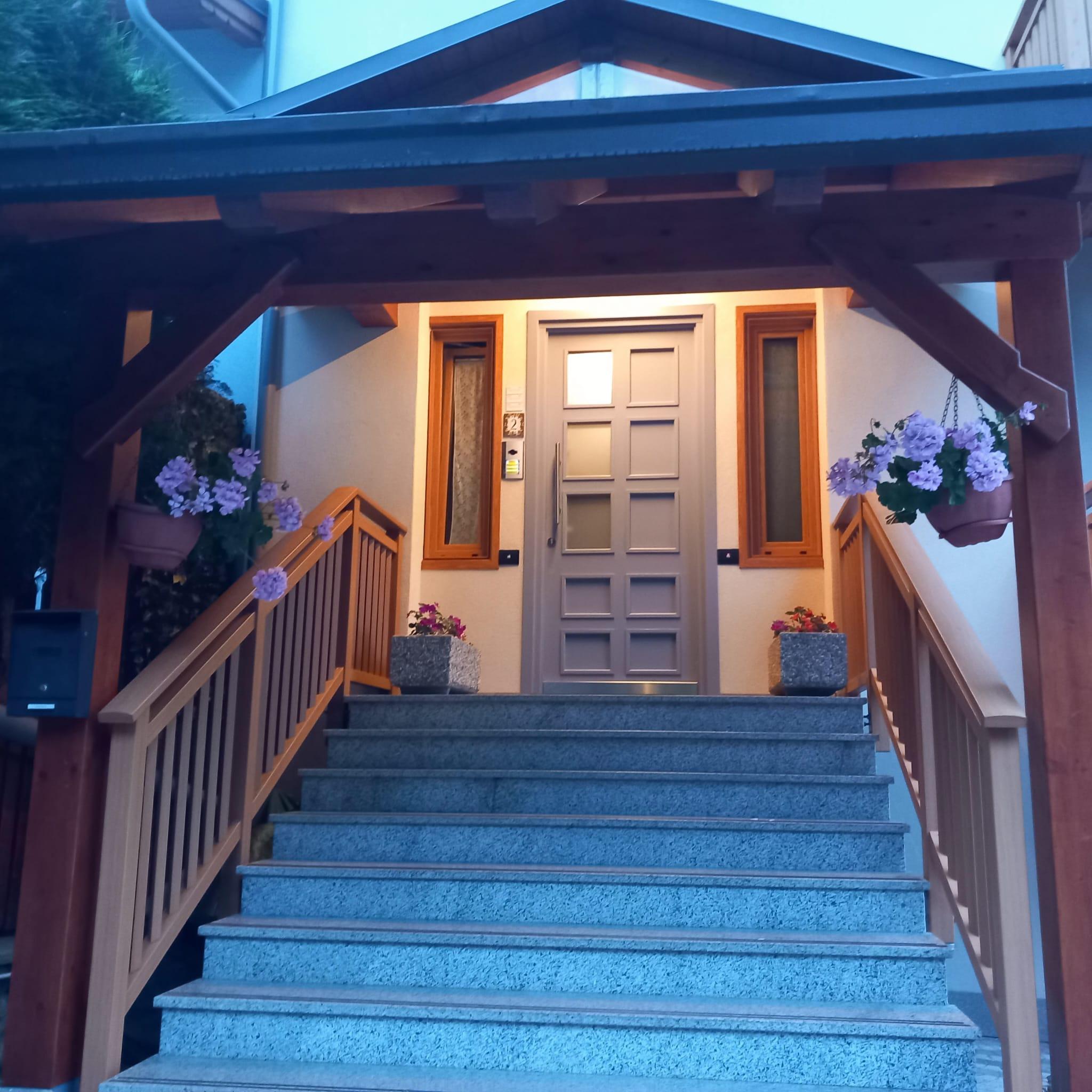 Una scalinata con parapetto in legno conduce a un ingresso elegante. Le fioriere con fiori colorati decorano l'area intorno alla porta.