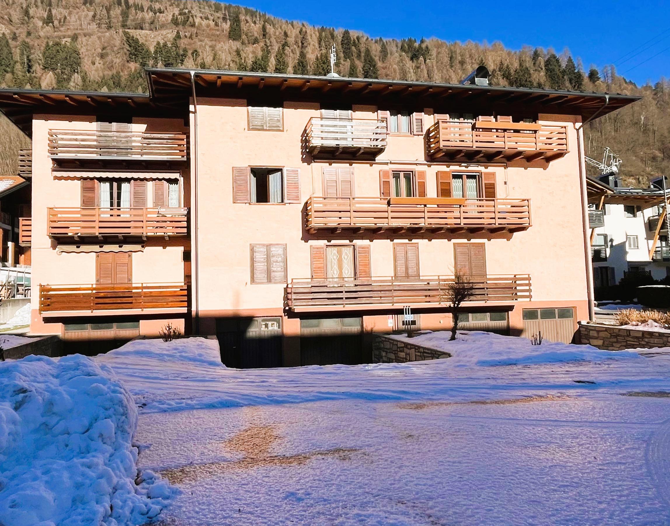 Ein Berggebäude mit Holzbalconys, umgeben von Schnee. Im Hintergrund gibt es Bäume und Berge.