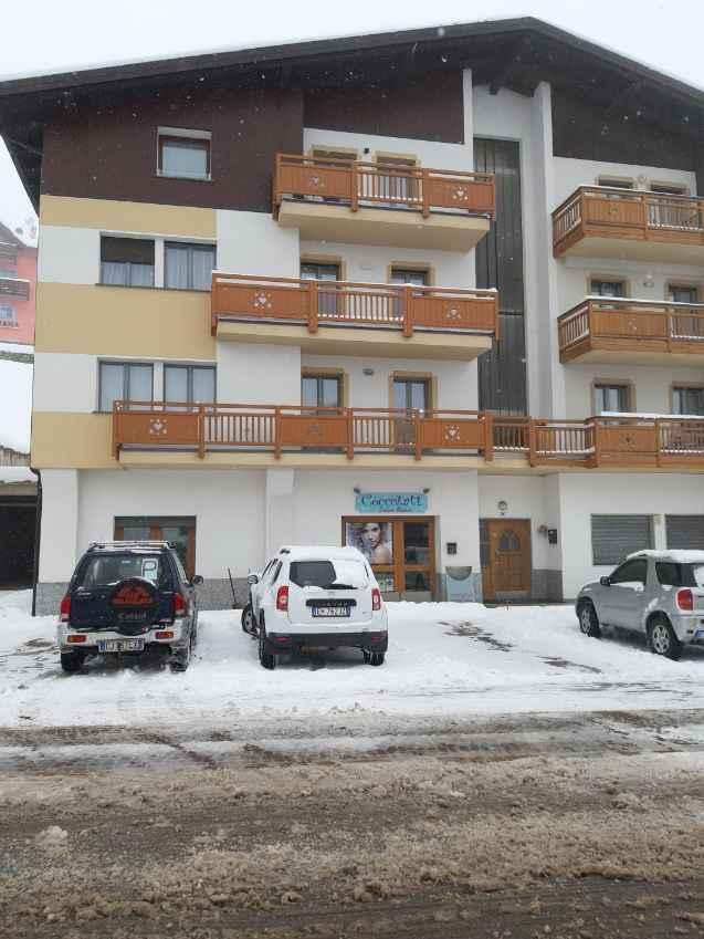 A building with wooden balconies, surrounded by snow. There are several cars parked on the snowy road.