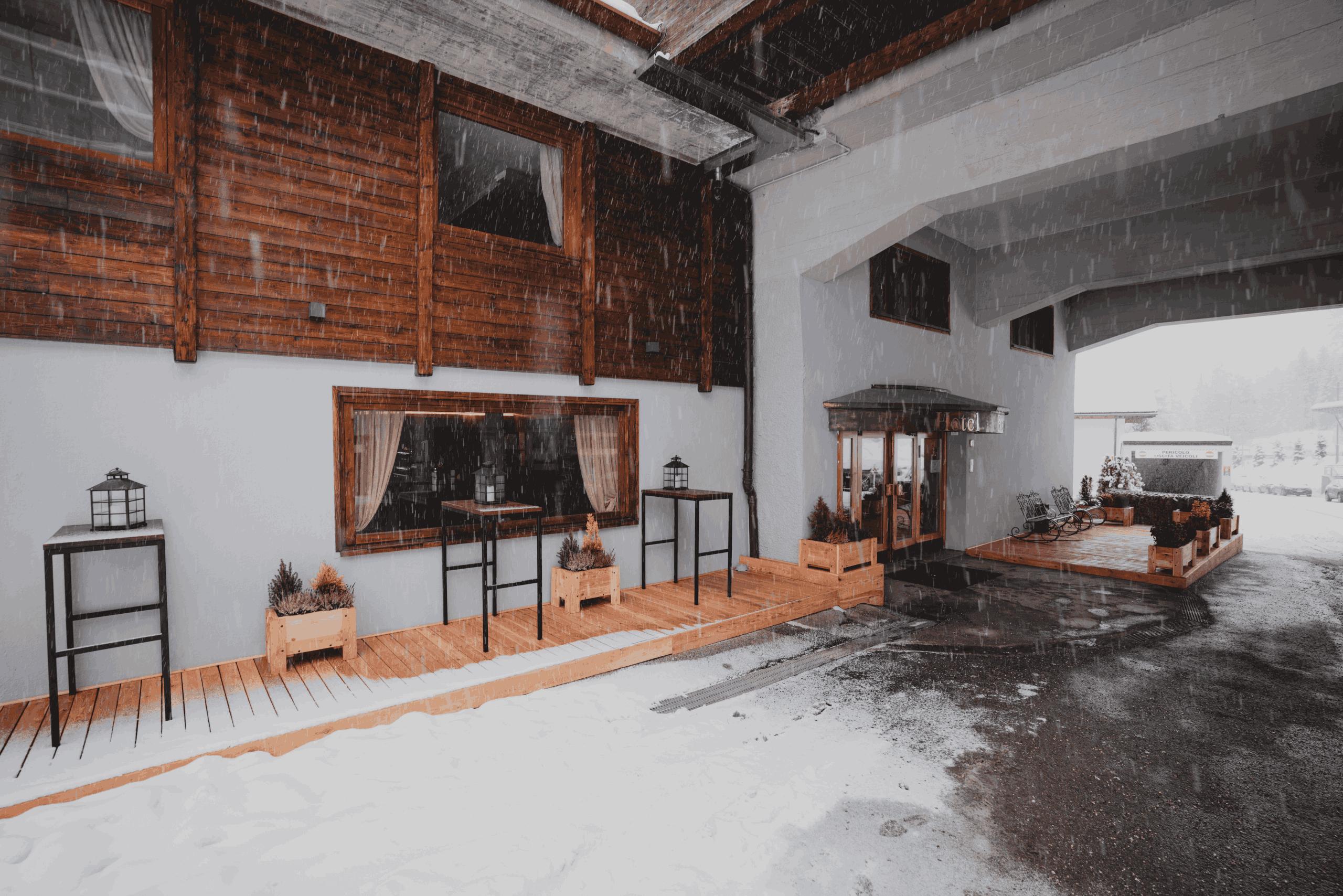 Un terrazzo elegante con tavoli in legno, immerso nella natura. Sullo sfondo si vedono montagne e un cielo sereno al tramonto.