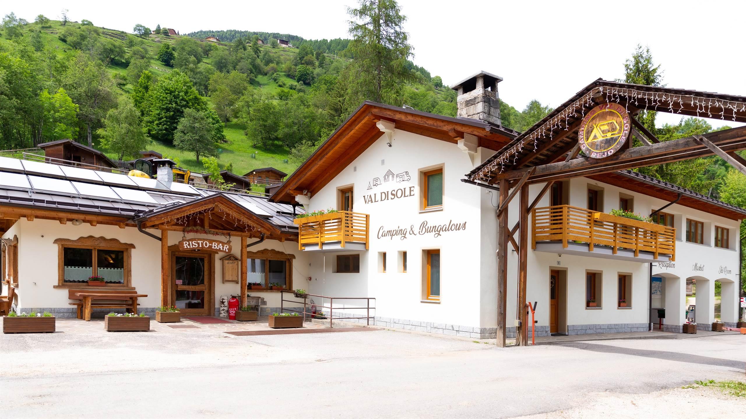 Un accogliente campeggio con ristorante in un contesto montano verde. La struttura è circondata da alberi e colline.