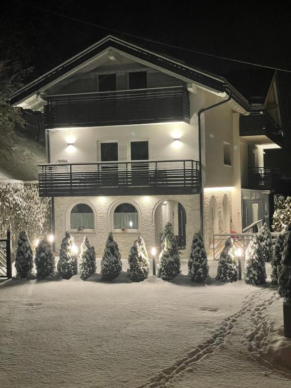 Una casa illuminata di notte, circondata da alberi di pino e coperta di neve. L'atmosfera è tranquilla e accogliente.