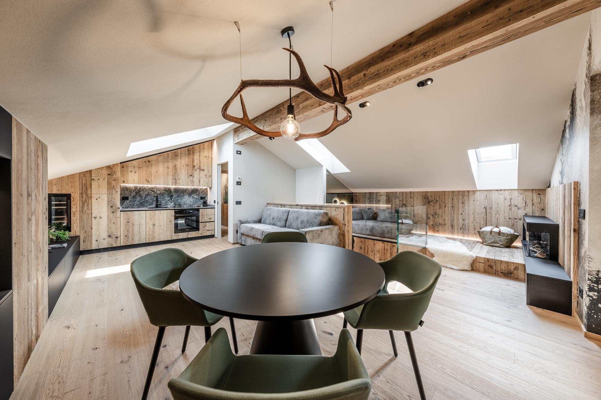 Una moderna mansarda con travi in legno e un arredamento accogliente. Un tavolo tondo al centro e un'illuminazione elegante creano un'atmosfera calda e invitante.