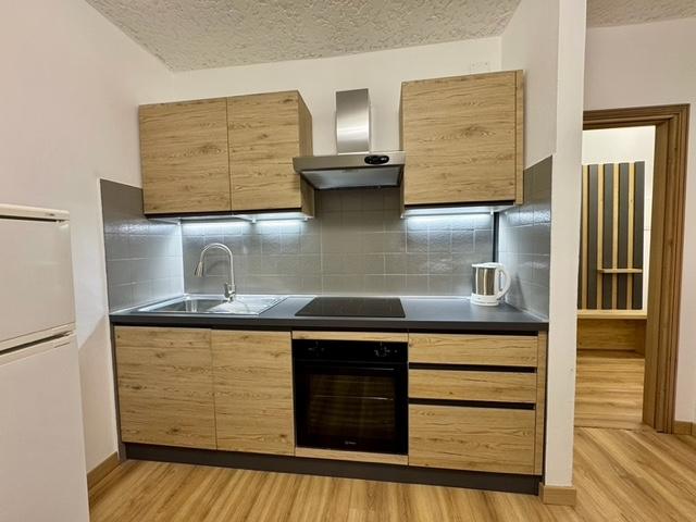 Una cucina moderna con mobili in legno e dettagli grigi. È dotata di piano cottura, lavello e elettrodomestici integri.