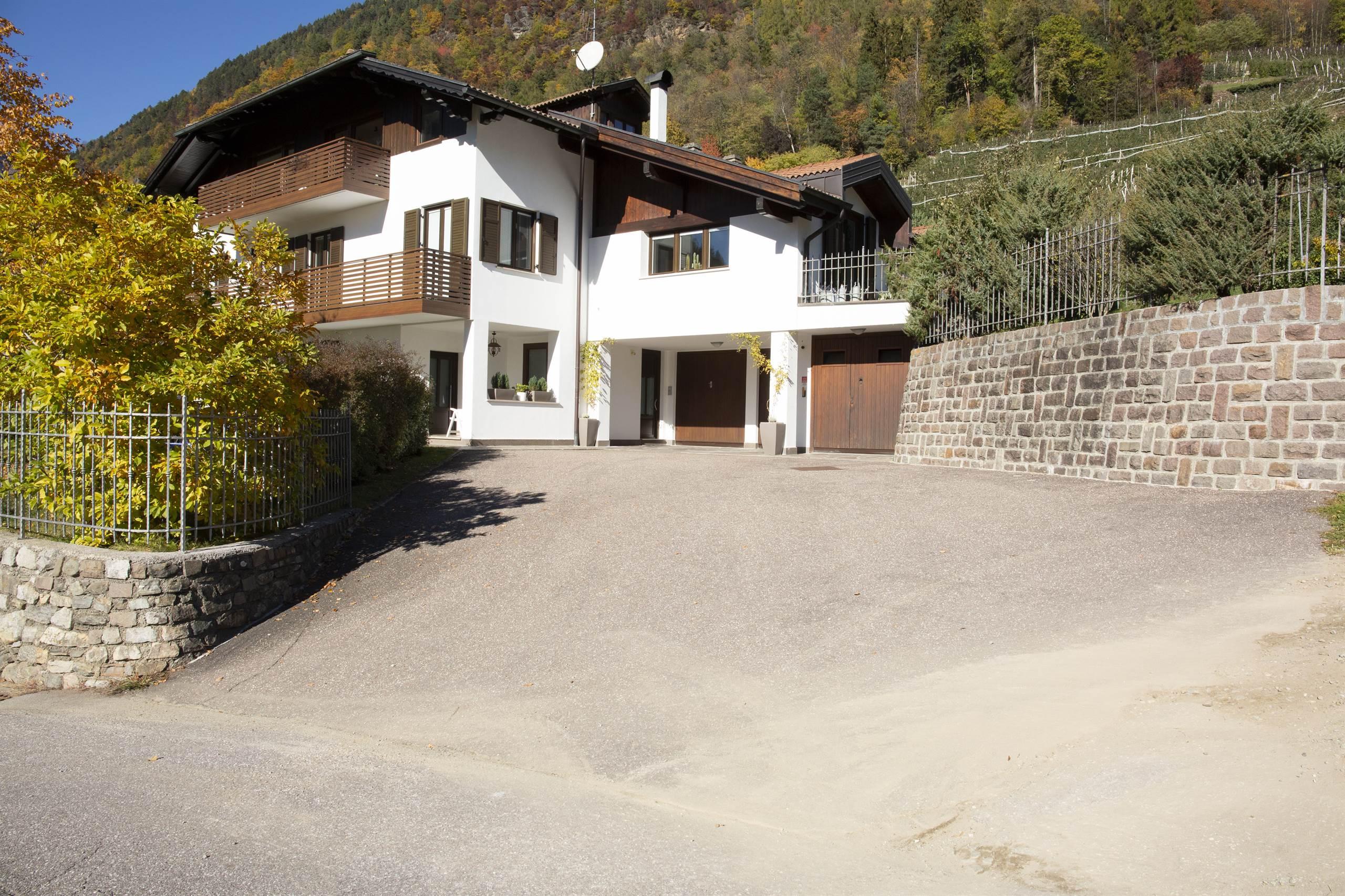 Ein modernes Haus mit elegantem Design, umgeben von einem gepflegten Garten. Es liegt in einer ruhigen, malerischen Gegend, mit Vegetation und Hügeln im Hintergrund.