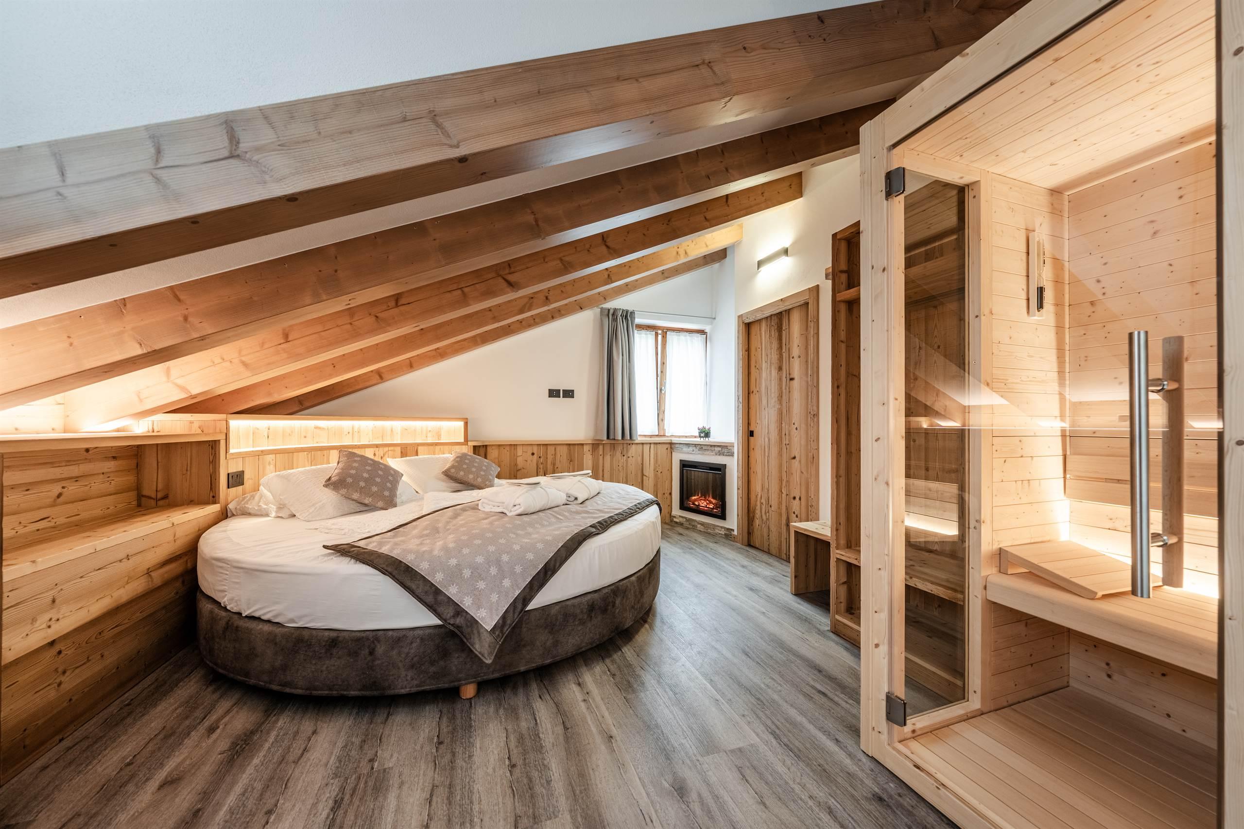 A cozy room with a slanted ceiling and exposed wood. There is a round bed and a sauna, creating a relaxing atmosphere.