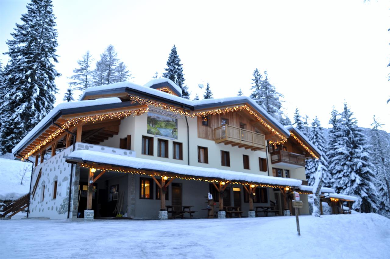 Una bella baita innevata con decorazioni luminose. Circondata da alberi e un’atmosfera invernale suggestiva.
