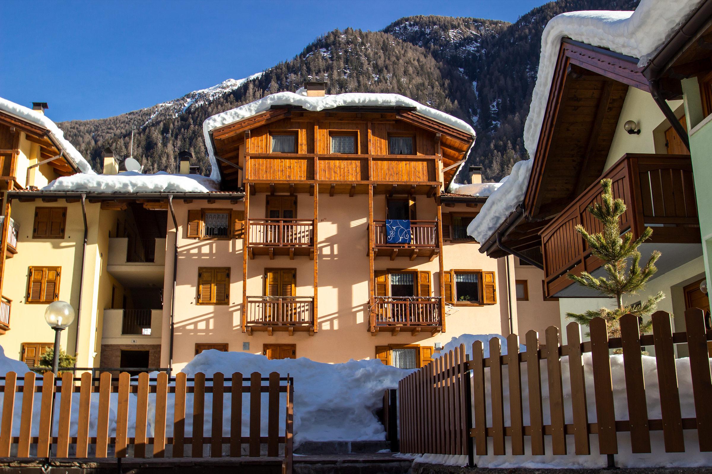 Un accogliente chalet di montagna con balconi in legno, circondato da neve fresca. Sullo sfondo si vedono le cime delle montagne.