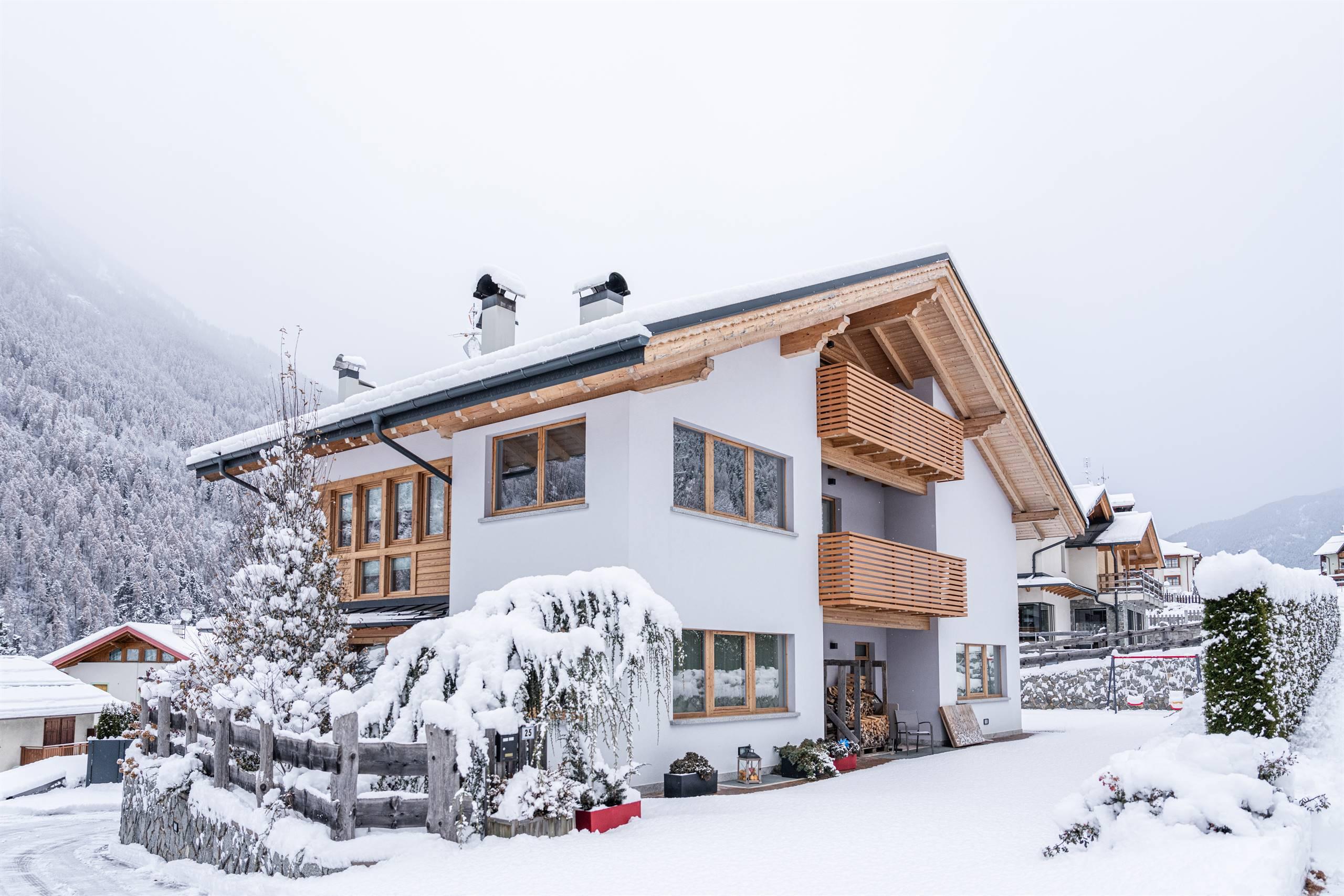 Una casa elegante in un paesaggio invernale, circondata da neve e alberi. Le montagne sullo sfondo completano la scena incantevole.