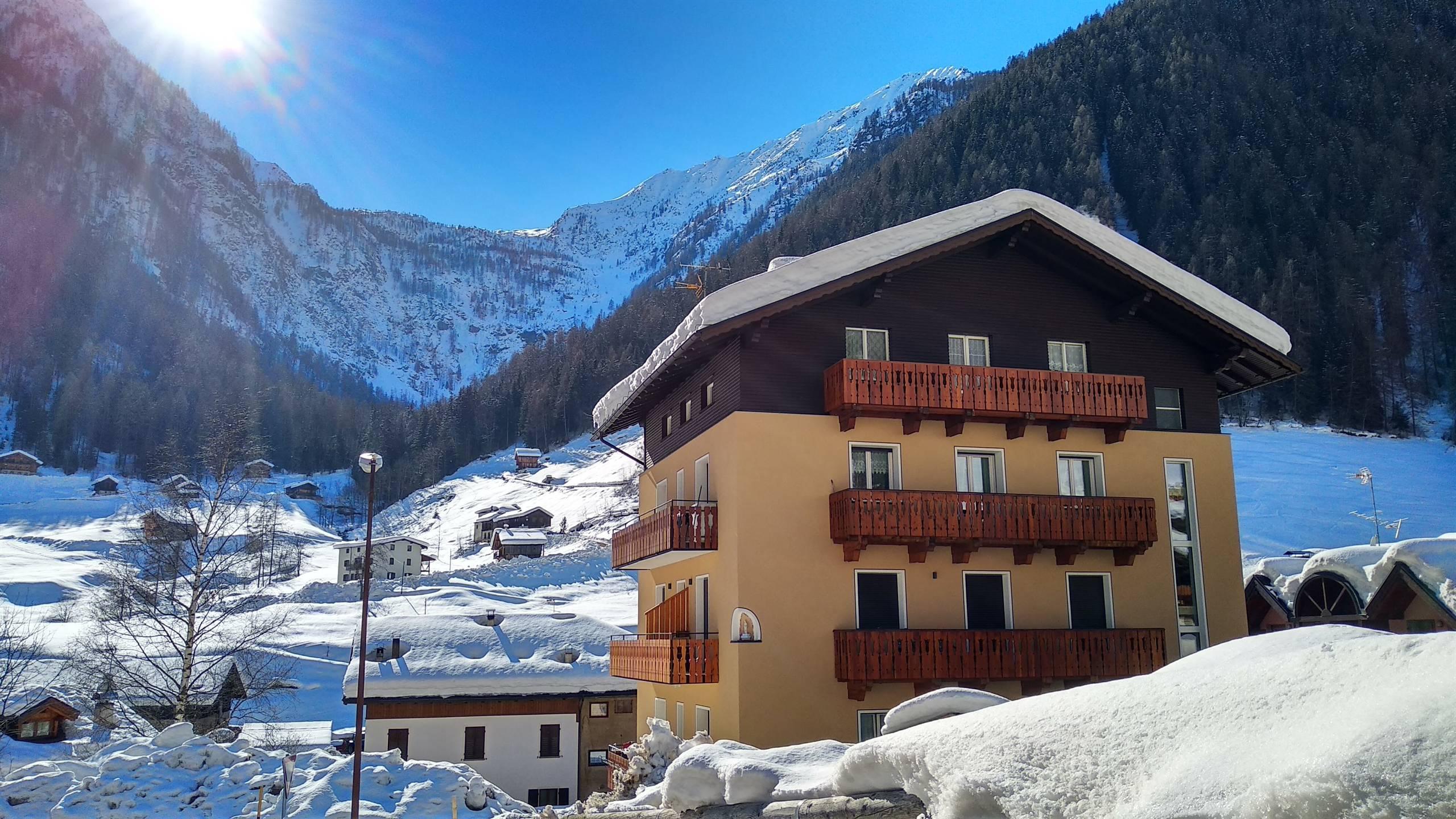A cabin in the mountains surrounded by beautiful fresh snow. In the background, the majestic mountains are illuminated by the sun.
