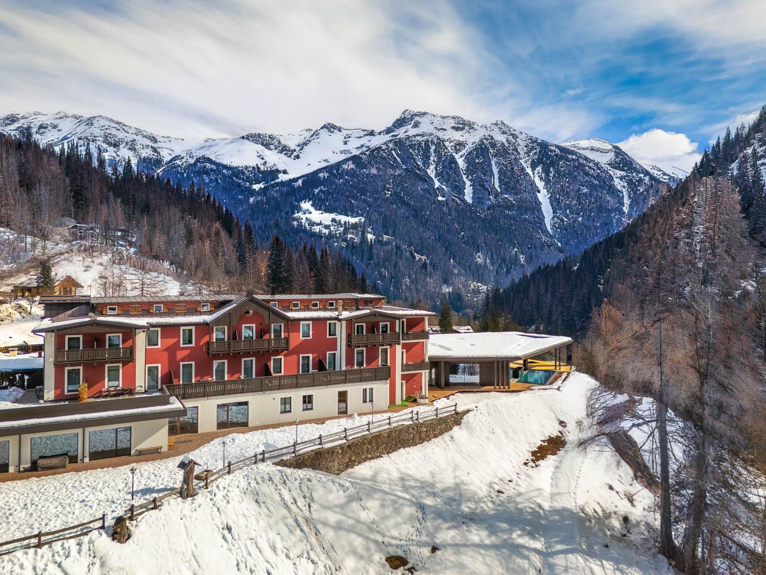 Ein gemütliches Hotel, umgeben von verschneiten Bergen und Bäumen. Der Himmel ist klar und die Berge erheben sich majestätisch im Hintergrund.