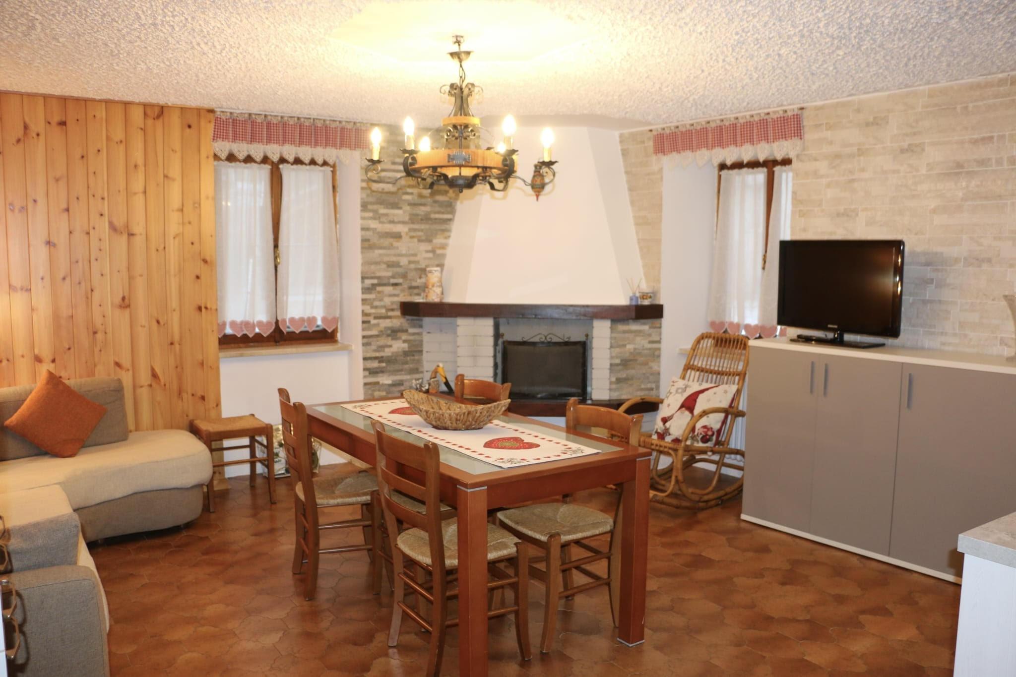 Ein gemütliches Wohnzimmer mit einem Holztisch und Stühlen. Der Raum ist von einem Kronleuchter beleuchtet und verfügt über einen Kamin und einen Fernseher.