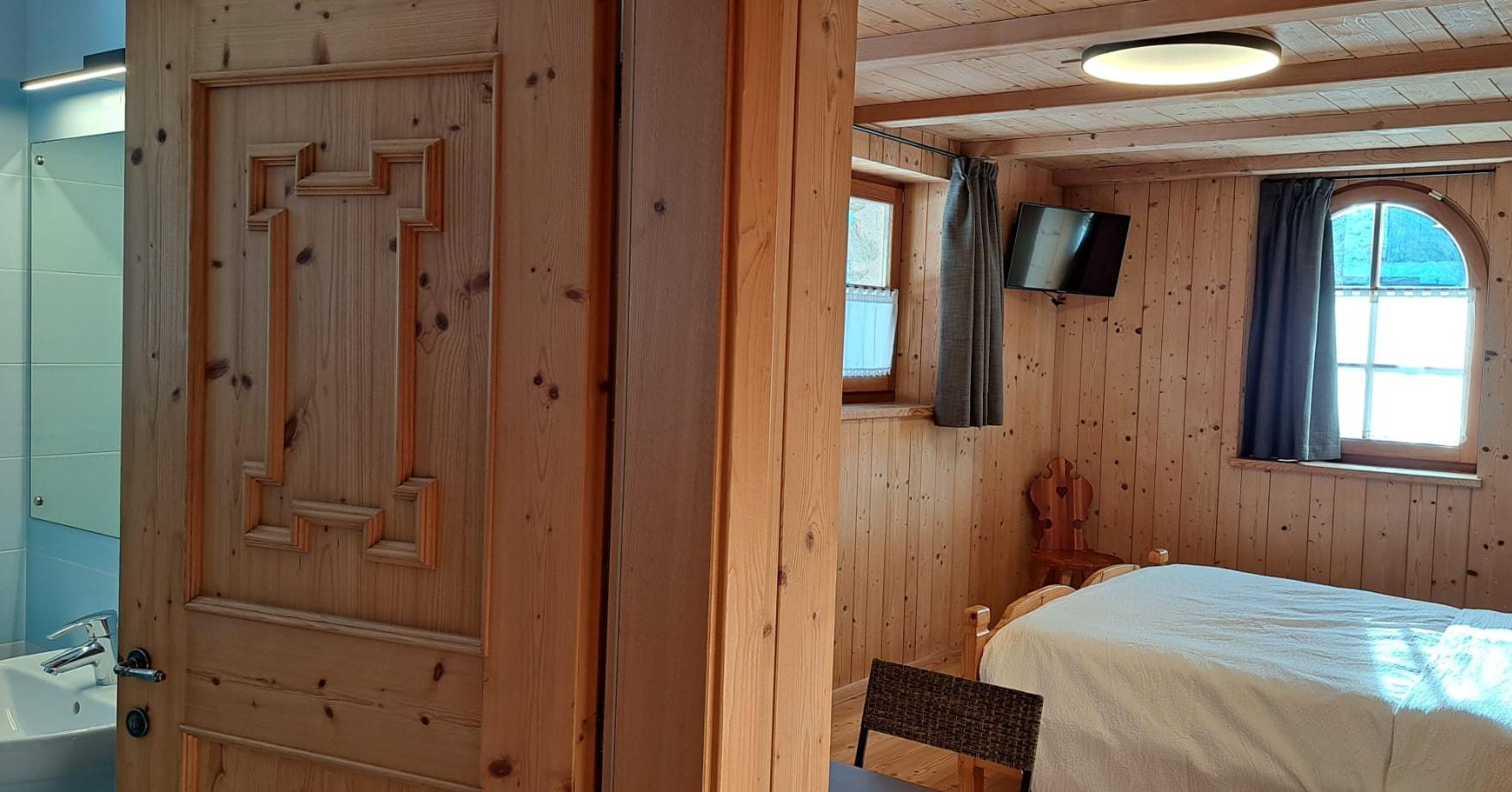 A cozy wooden room, with an arched window and a double bed. There is also an adjoining bathroom and a wall-mounted television.