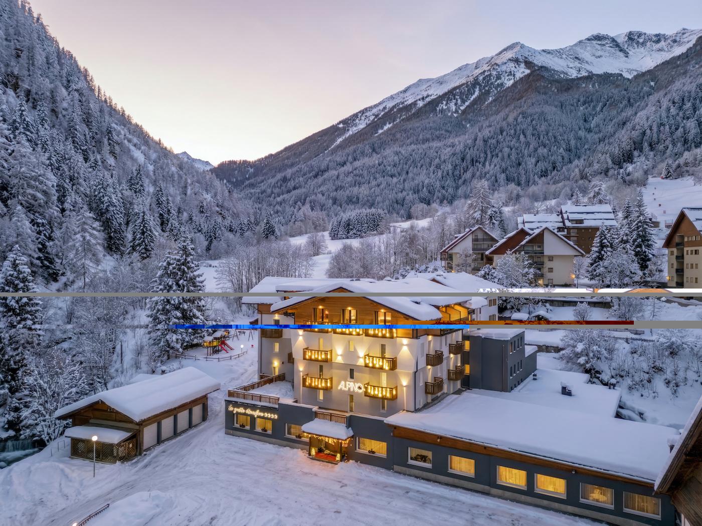Una montagna innevata con un hotel accogliente in primo piano. L'atmosfera è tranquilla e incantevole, circondata da alberi e prati bianchi.