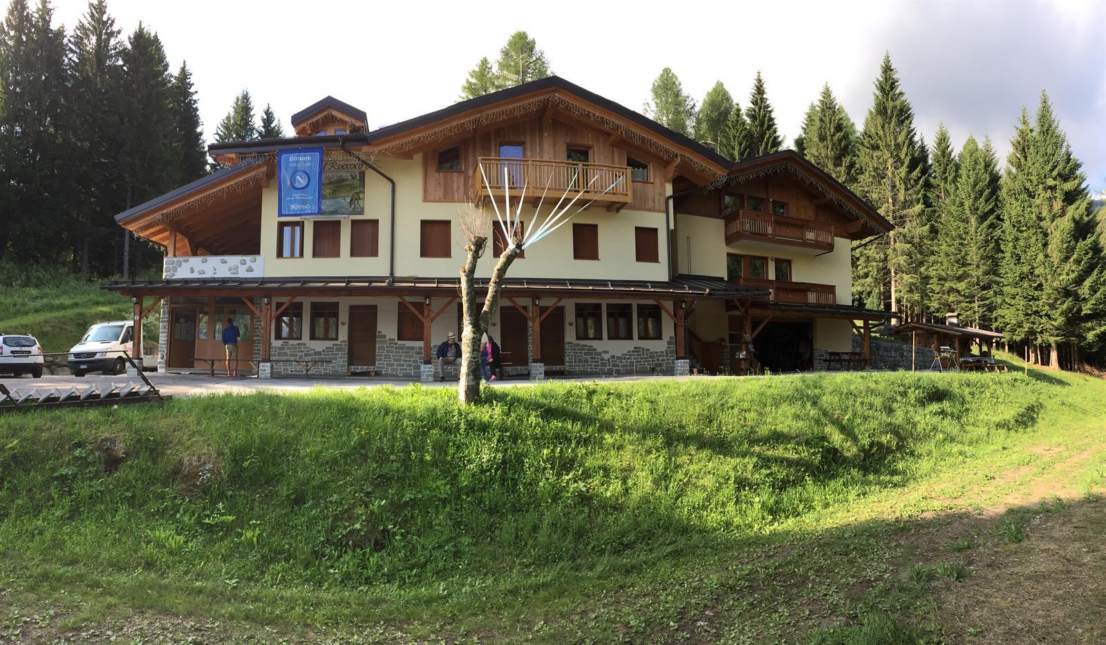 Una montagna con una baita in legno circondata da alberi sempreverdi. L'edificio ha un design tradizionale e accogliente, con un ampio giardino di fronte.