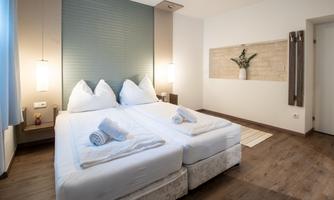 A modern room with two single beds and fresh towels. The walls are in neutral colors and there are decorative elements like plants.