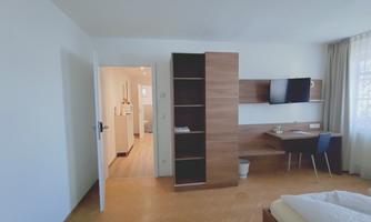 A modern room with a desk, a television, and a wardrobe. The floor is made of wood and the walls are painted light.