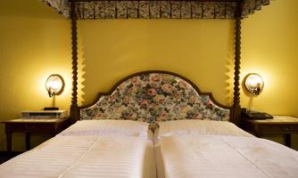 A cozy bedroom with two single beds and a colorful headboard strip. The walls are painted yellow and there are stylish bedside lamps.