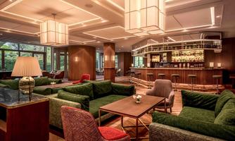 An elegant lounge area with cozy green sofas and a stylish bar area. Soft lighting and modern design elements create an inviting atmosphere.