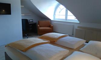 A cozy room with two beds and a window that lets in a lot of light. There is a desk and an orange armchair for relaxation.